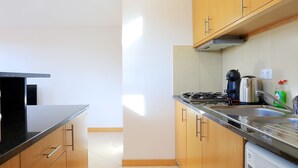 Una cocina compacta con armarios de madera, lavadora integrada y una encimera con hervidor y cafetera.