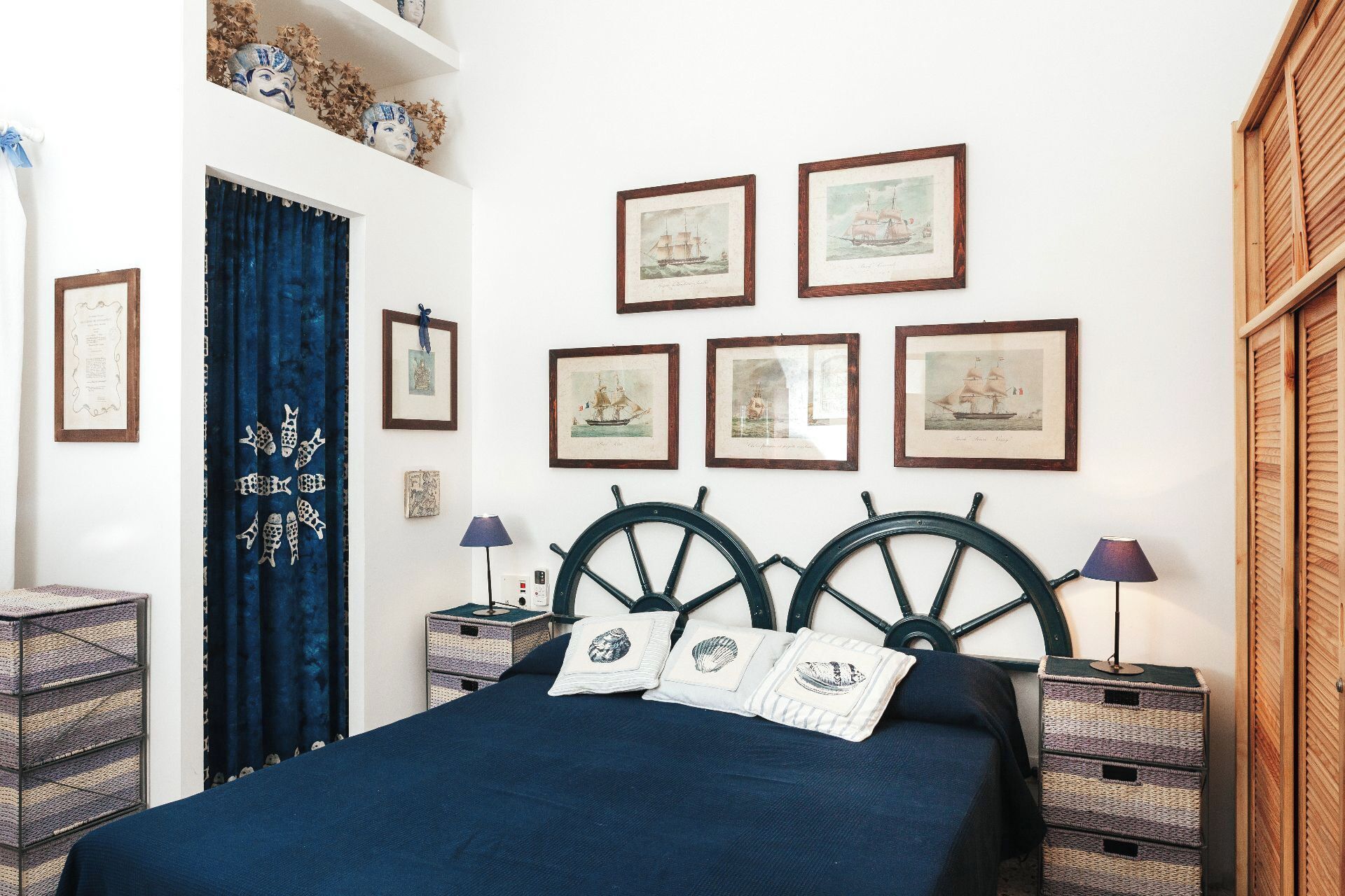 Un dormitorio con cama, cabecera, mesitas de noche, lámparas y cuadros en la pared.