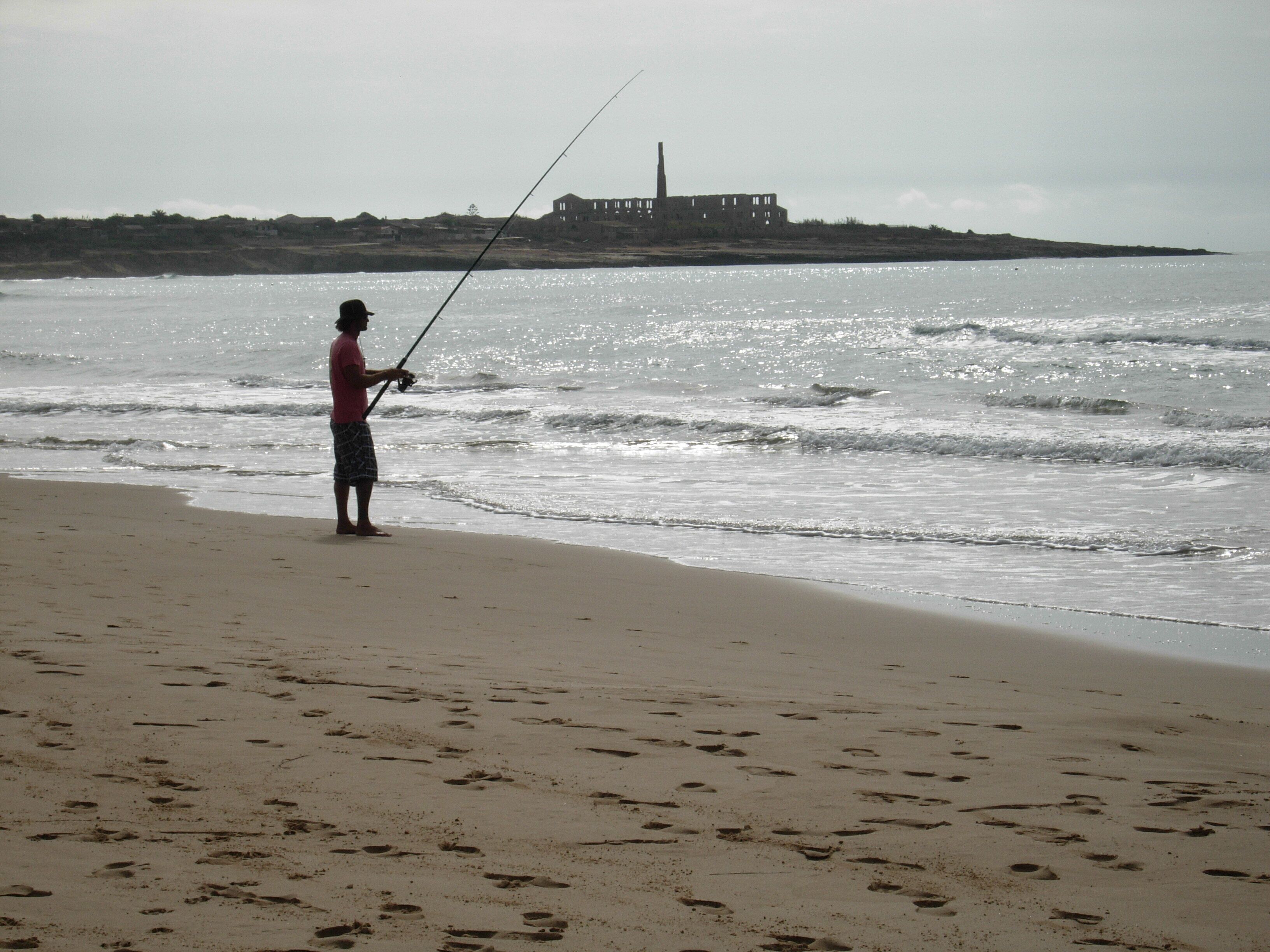 A beach with footprints and a person fishing.