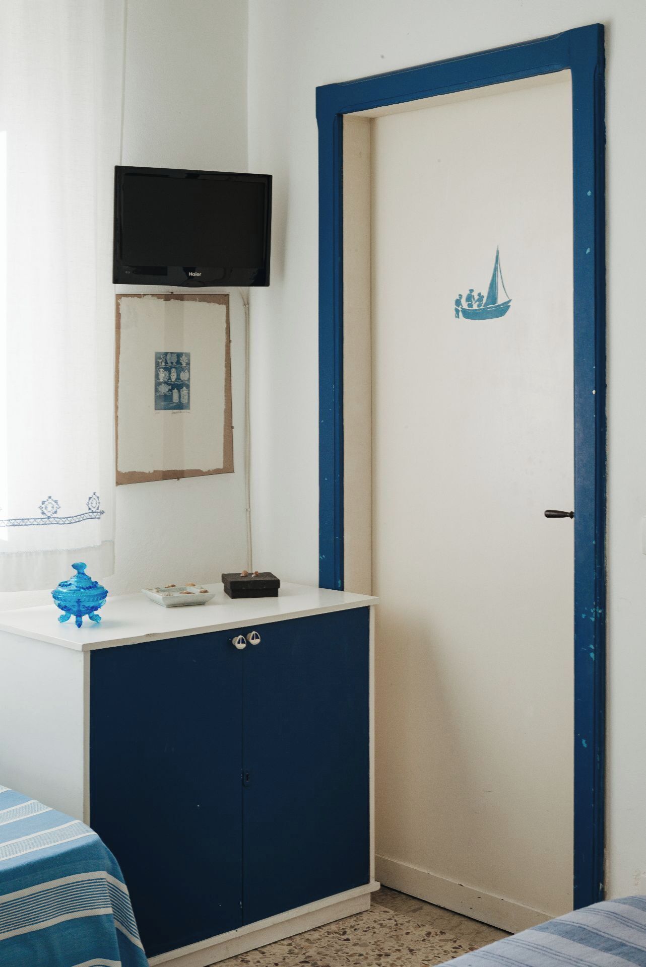 A room with a white and blue door, a small cabinet with a television above it, and a framed picture on the wall.
