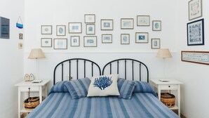 A bedroom with a bed, two nightstands, a wall with framed pictures, and a white wall. - Seaside house - Casazzurra, Sicily (Sampieri)
