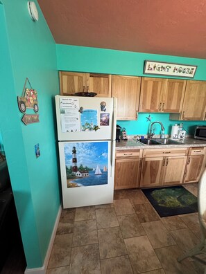 Una cocina con armarios de madera, un refrigerador con imanes y notas, un lavamanos y una pared color turquesa.