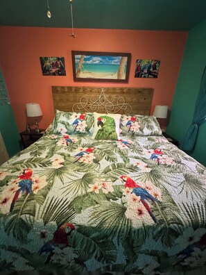 Una cama con colcha de motivos tropicales, cabecera de madera y dos lámparas de noche.