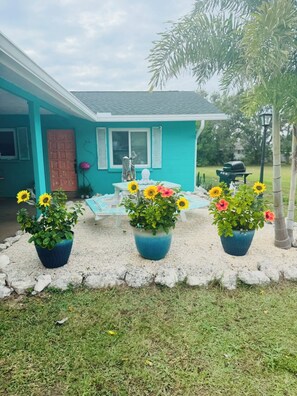 Una casa con fachada azul, una puerta roja y tres girasoles en macetas al frente.