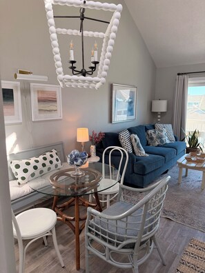 A living room with a blue sofa, white chairs, a glass coffee table, and a chandelier.