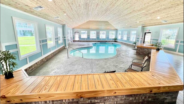 Un vaste espace intérieur abritant une piscine, avec un plafond en bois, de grandes fenêtres et un comptoir d’accueil.