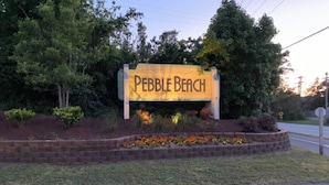 Un panneau en bois sur lequel est inscrit « Pebble Beach », entouré de parterres et d’arbres aménagés.
