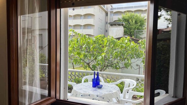 A window with a view of a balcony area, featuring a table with chairs and a blue vase. - Holiday apartment with open terrace and air conditioning (Lignano)