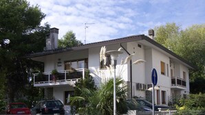 A two-story building with a balcony, a sign indicating a no parking zone, and a blue directional sign. - Holiday apartment with open terrace and air conditioning (Lignano)