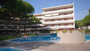 A hotel with a swimming pool, multiple balconies, and a landscaped garden area. - Holiday apartment with balcony and pool (Lignano)