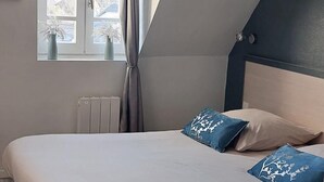 Een slaapkamer met een bed, een raam met gordijnen, een radiator en een pluizig vloerkleed.