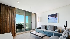 A modern living room with a sofa, coffee table, and a view of the outdoors through a sliding glass door. - Swainson at Embassy - 917 (Adelaide)
