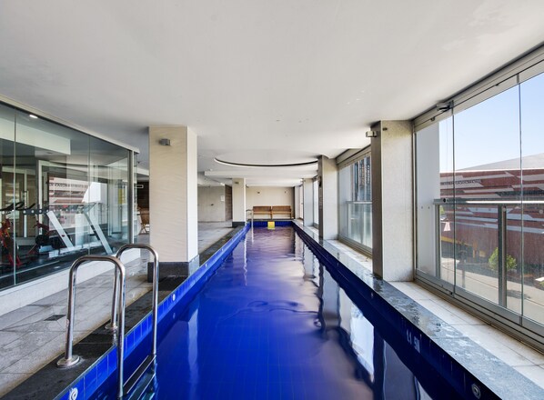 A long indoor swimming pool with clear glass walls on one side and a bench in the center.