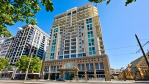 A multi-story hotel with a modern design, featuring balconies, large windows, and a ground-level coffee shop. - Swainson at Embassy - 917 (Adelaide)