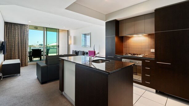A modern kitchen with dark cabinetry, a central island, and a dining area with a view. - Swainson at Embassy - 917 (Adelaide)