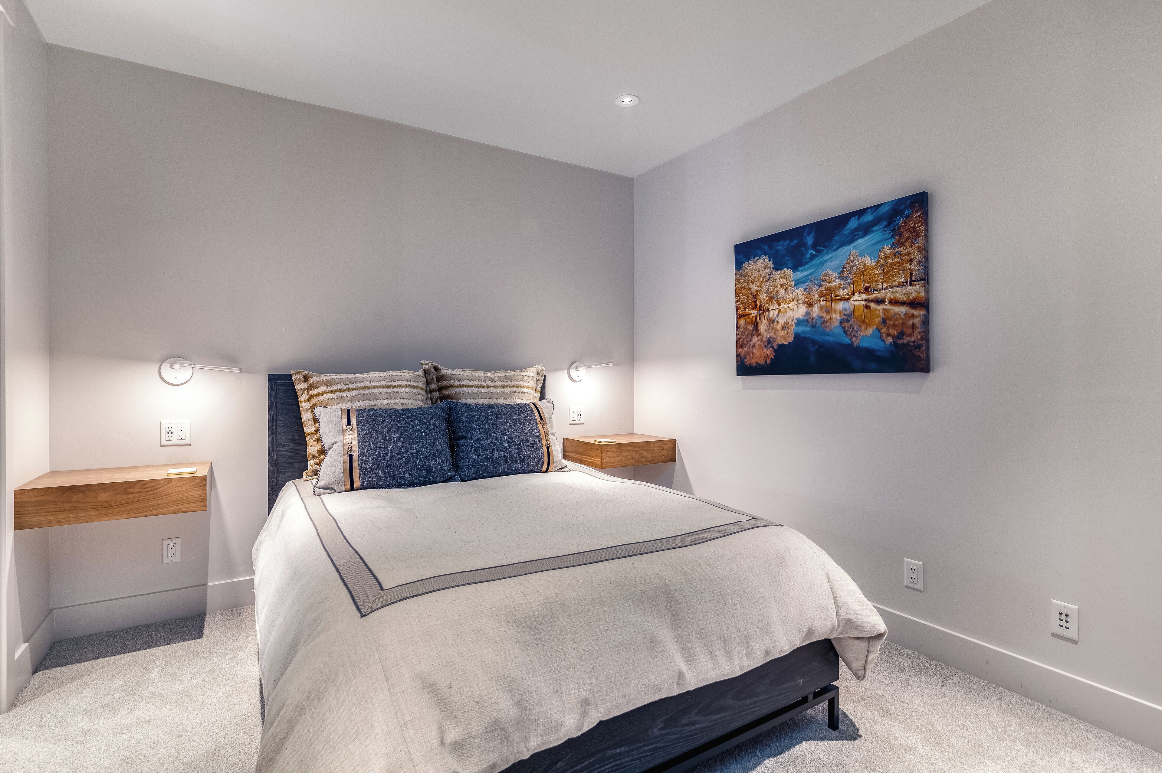 A bedroom with a bed, nightstands, a wall-mounted painting, and a built-in bench.