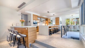 A modern kitchen with a central island, bar stools, and a staircase leading to an upper level.