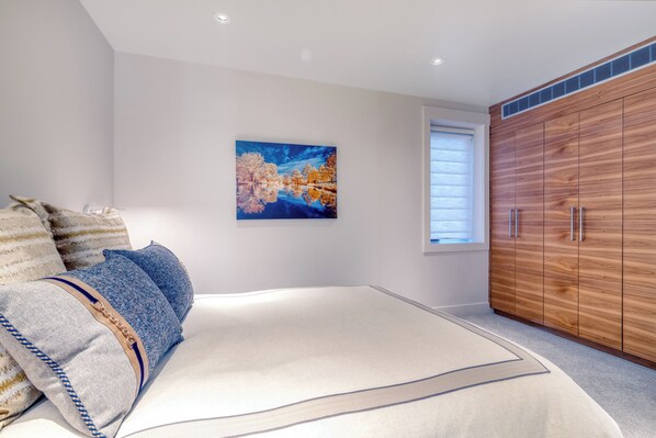 Une chambre avec un grand lit, une armoire en bois, un tableau au mur et une fenêtre avec des stores.