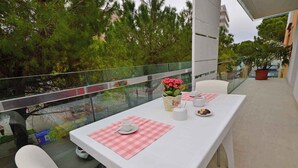 Un balcon avec une table blanche dressée pour deux personnes, une balustrade en verre et une vue sur les arbres et les bâtiments.