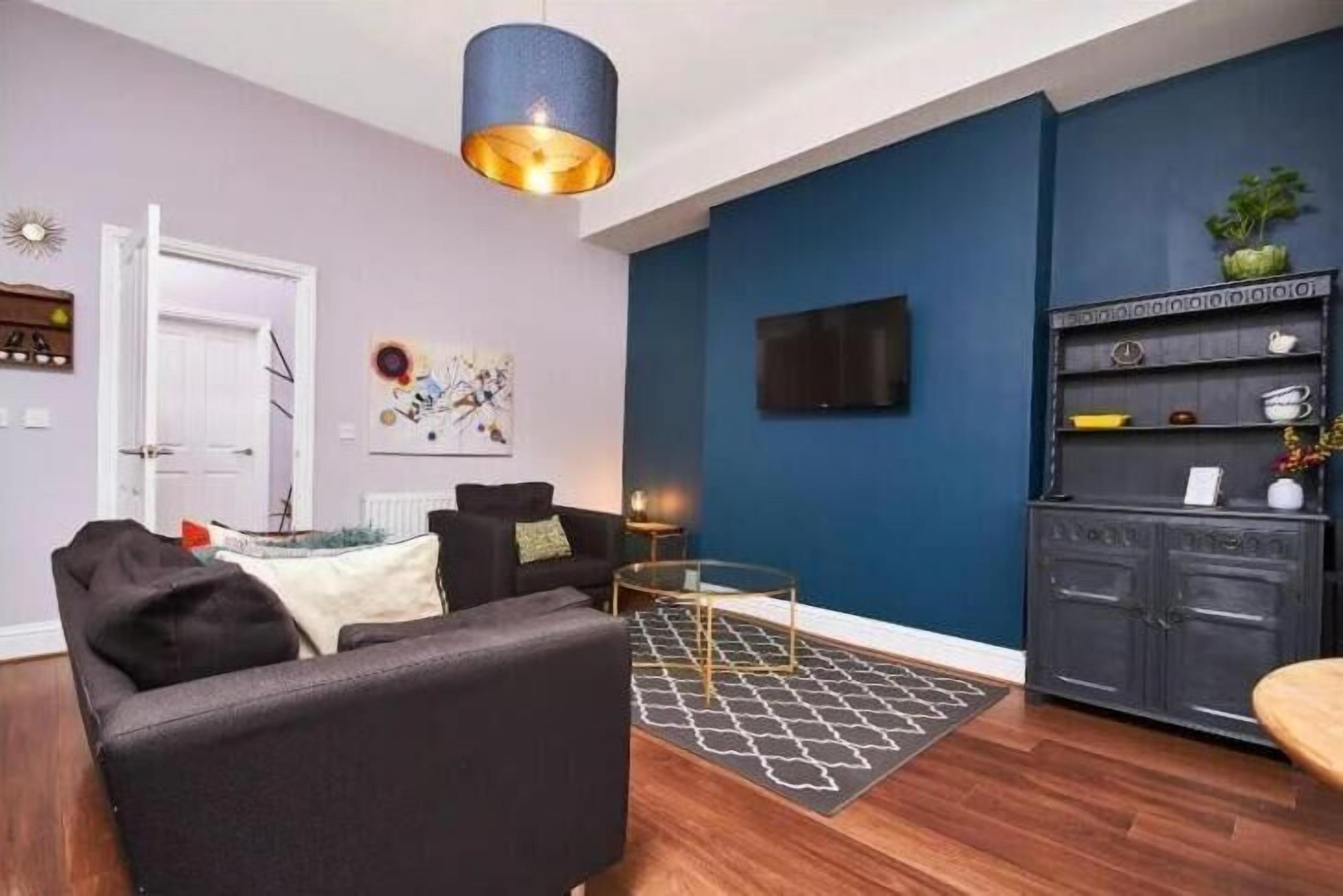 Un salon moderne avec un mur d’accent bleu foncé, un canapé noir, une table basse en verre et un tapis à motifs.