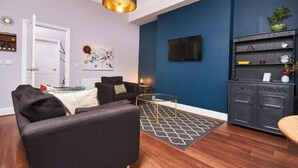 Una sala de estar moderna con una pared azul oscuro de acento, un sofá negro, una mesa de centro de vidrio y una alfombra estampada.