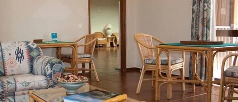 A living room with a sofa, a coffee table with books, and wicker chairs.