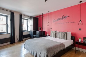 Un dormitorio moderno con una cama grande, un escritorio y una pared de acento roja con texto motivacional.