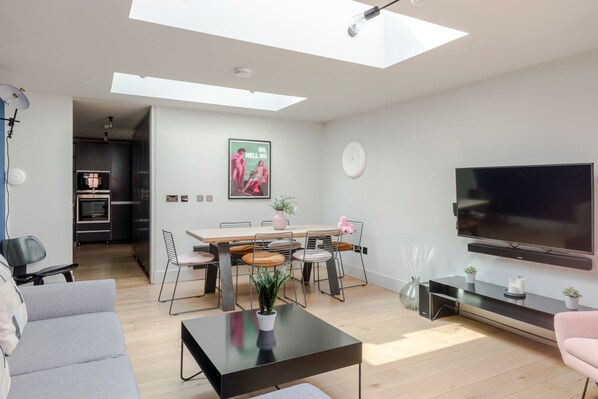 A modern living room with a dining area, a flat-screen TV, and a skylight.