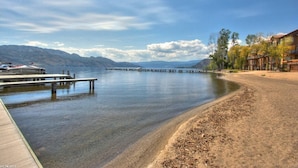 Ein Anwesen am See mit einem hölzernen Steg, der in ruhiges Wasser führt, umgeben von Bergen und einer Reihe von Gebäuden mit Balkonen.