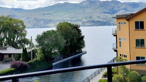 Blick auf einen See mit einem Gebäude, das Balkone und eine klare Sicht auf See und Berge bietet.