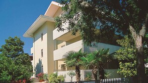 Un immeuble à plusieurs étages doté de balcons, entouré d’arbres et d’un mur de pierre.