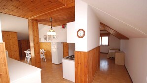 Une cuisine spacieuse agrémentée de touches de bois, un coin repas avec des chaises blanches et un espace nuit confortable avec un lit et une petite table.