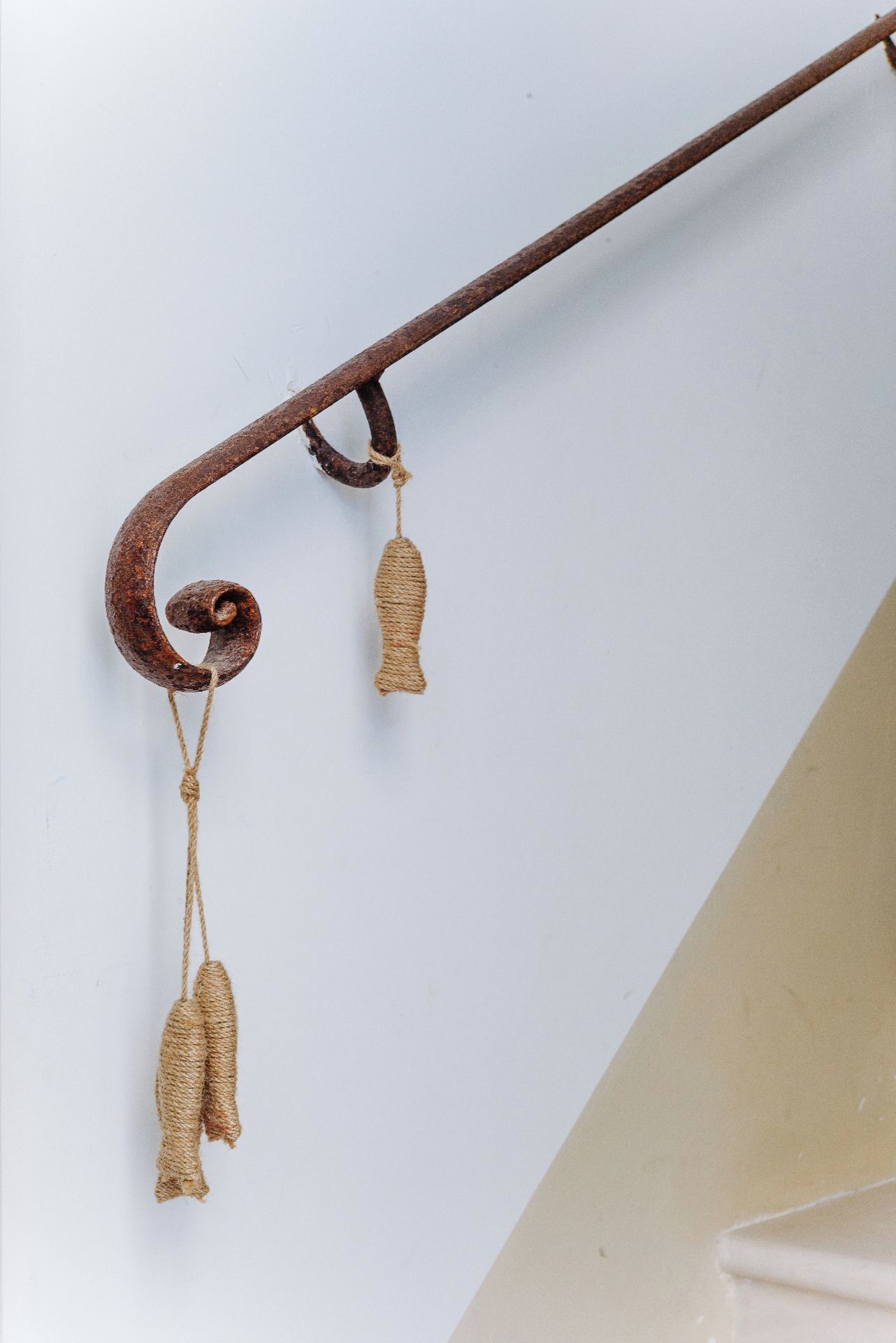 Un crochet en métal de style rustique, orné de deux pompons en corde qui y sont suspendus.