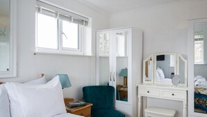 Ett sovrum med en säng, ett skrivbord med en spegel, en stol och ett fönster med persienner.