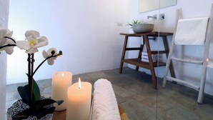 Un baño con un lavamanos blanco, un espejo, una silla de madera y una toalla blanca colgada en la pared.
