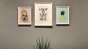 Un coin repas avec une table, des chaises et une plante en pot. Trois tableaux encadrés sont accrochés au mur au-dessus de la table.
