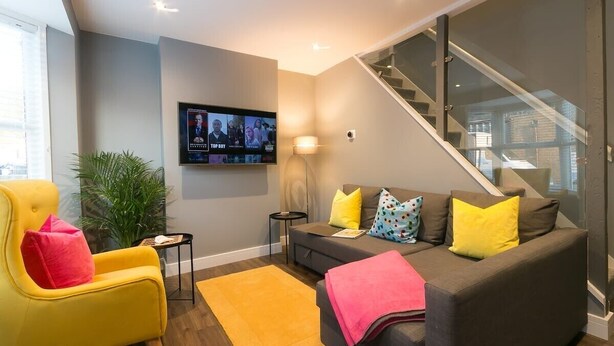 Un salon moderne avec un canapé, un fauteuil et un téléviseur fixé au mur.