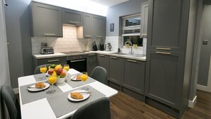 Une cuisine moderne avec des meubles gris, un plan de travail blanc et une table à manger dressée pour le petit-déjeuner.