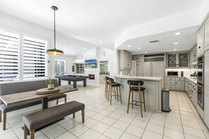 Une cuisine spacieuse avec des meubles blancs, un coin repas avec un banc et un bar avec des tabourets.