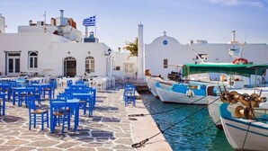 A coastal scene with white buildings, blue chairs, and boats docked by the water. - Santa Maria Studio 5 Mins From the Beach (Paros)
