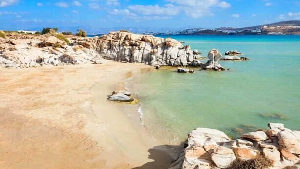 A coastal landscape with clear turquoise water, rocky formations, and a sandy beach. - Santa Maria Studio 5 Mins From the Beach (Paros)