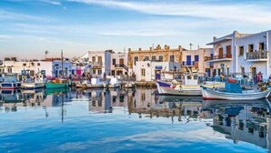 A harbor with boats docked, buildings with balconies, and a calm water surface reflecting the structures. - Santa Maria Studio 5 Mins From the Beach (Paros)
