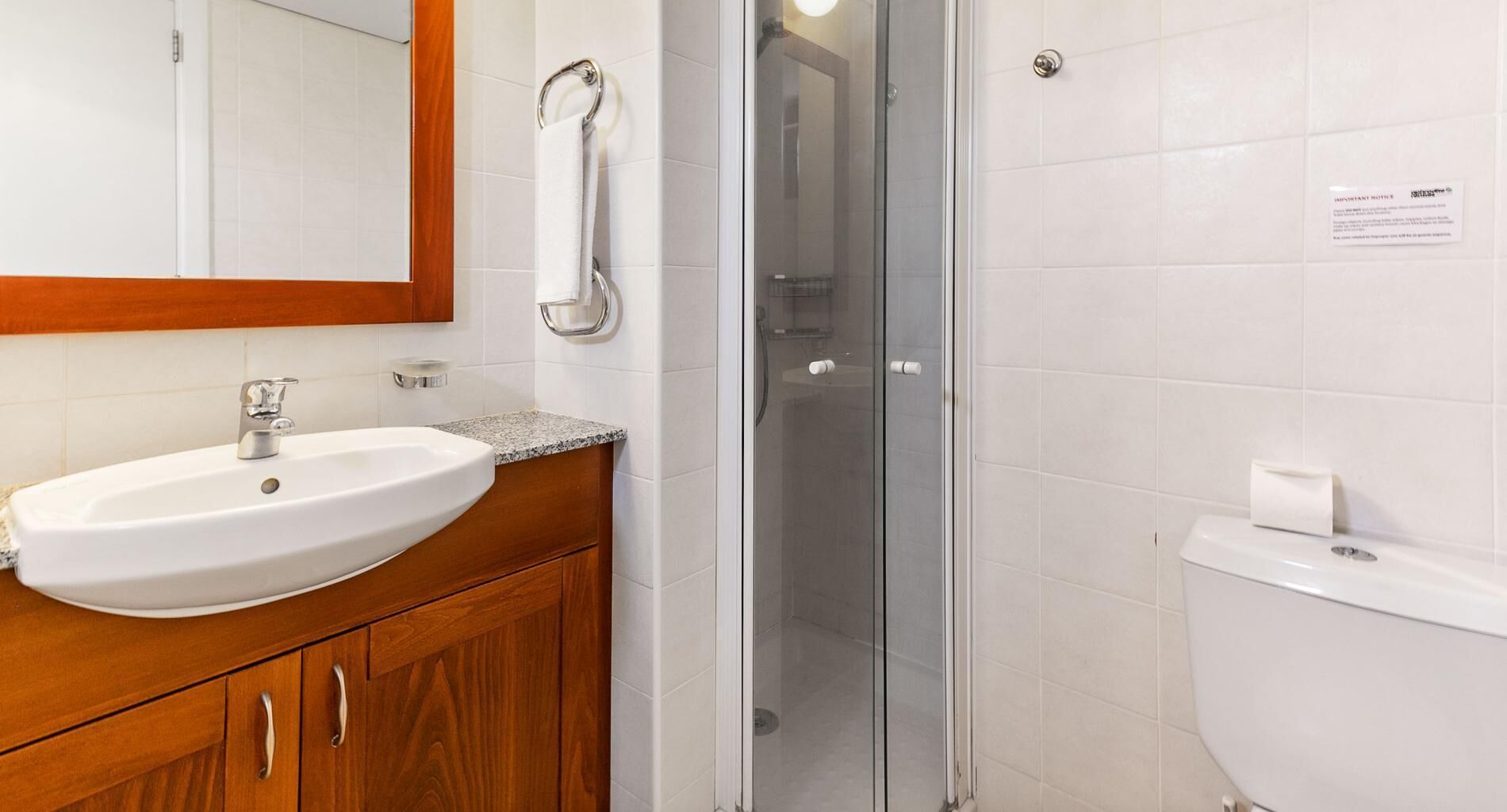 A bathroom with a white sink, wooden vanity, a glass shower enclosure, and a toilet.