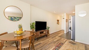 A modern living room with a wooden dining table, a flat-screen TV, and a large mirror. - Waikiki Moana Inn (Honolulu)