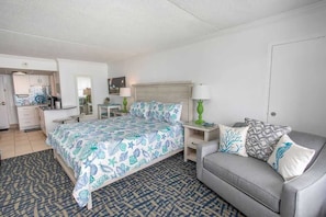 A hotel room with a bed, a grey sofa, a nightstand, a lamp, and a small table.