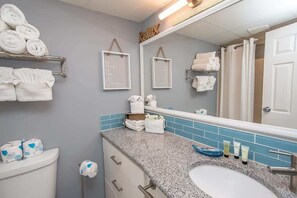 A bathroom with a granite countertop, white sink, and a large mirror. There are towels and toiletries on the counter.