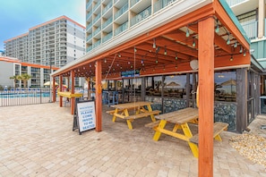 A beachfront restaurant with outdoor seating, a sign indicating a beachfront location, and a pool in the background.