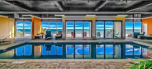 A pool area with a view of the ocean, a lounge with chairs, and a door leading to a balcony.