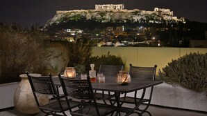 Ein Außenbereich zum Essen mit Tisch und Stühlen, einer großen Vase und Blick auf ein historisches Gebäude bei Nacht.
