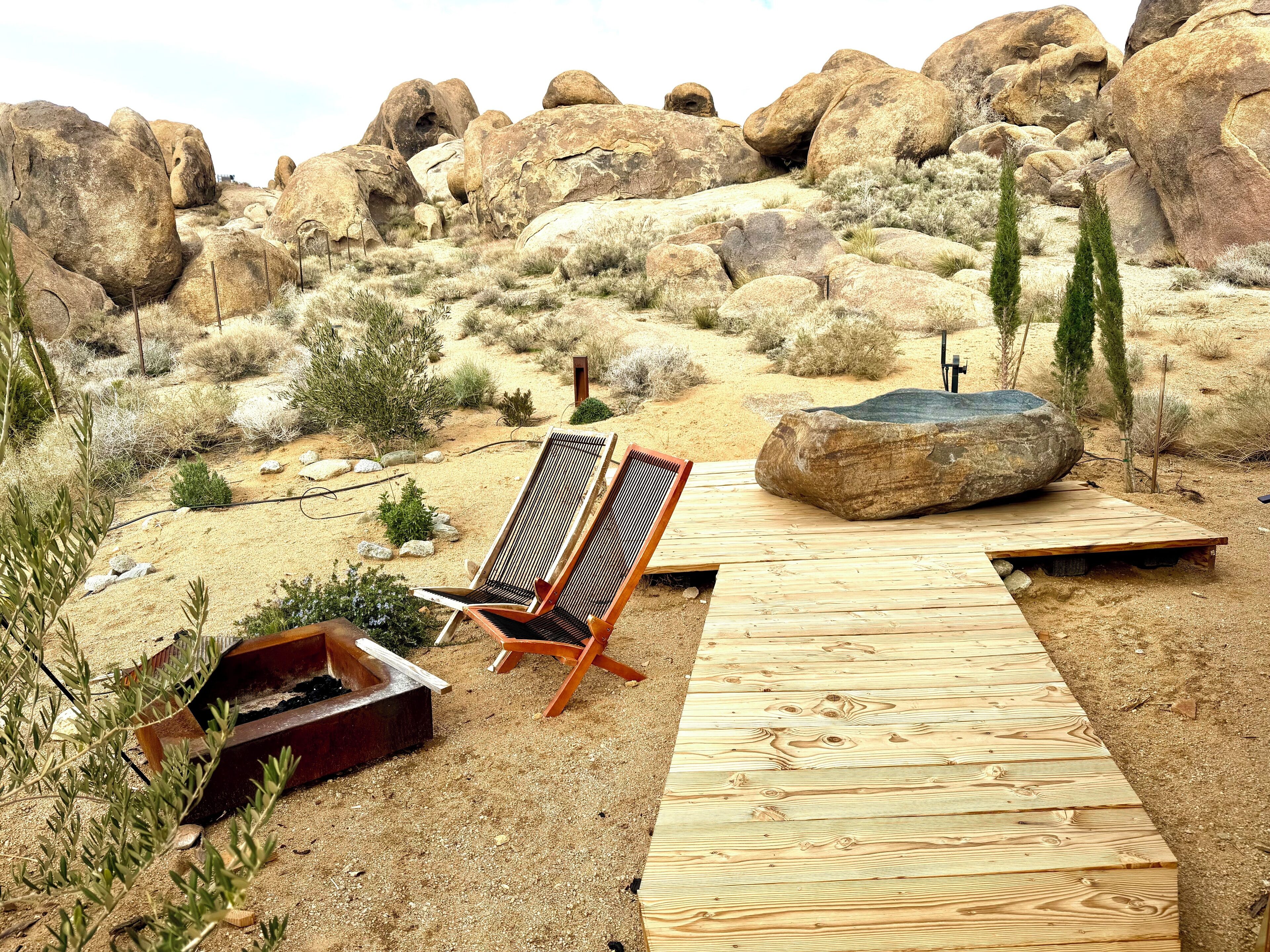 Une terrasse en bois avec deux chaises longues, un foyer et une vue sur un paysage rocheux.